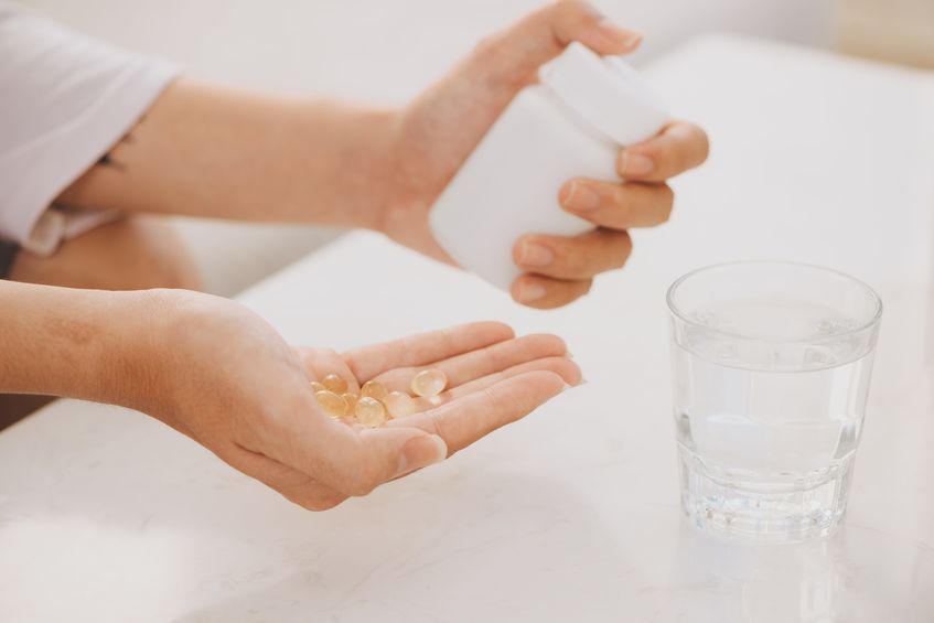 A woman's hand taking healthy supplements with a glass of water